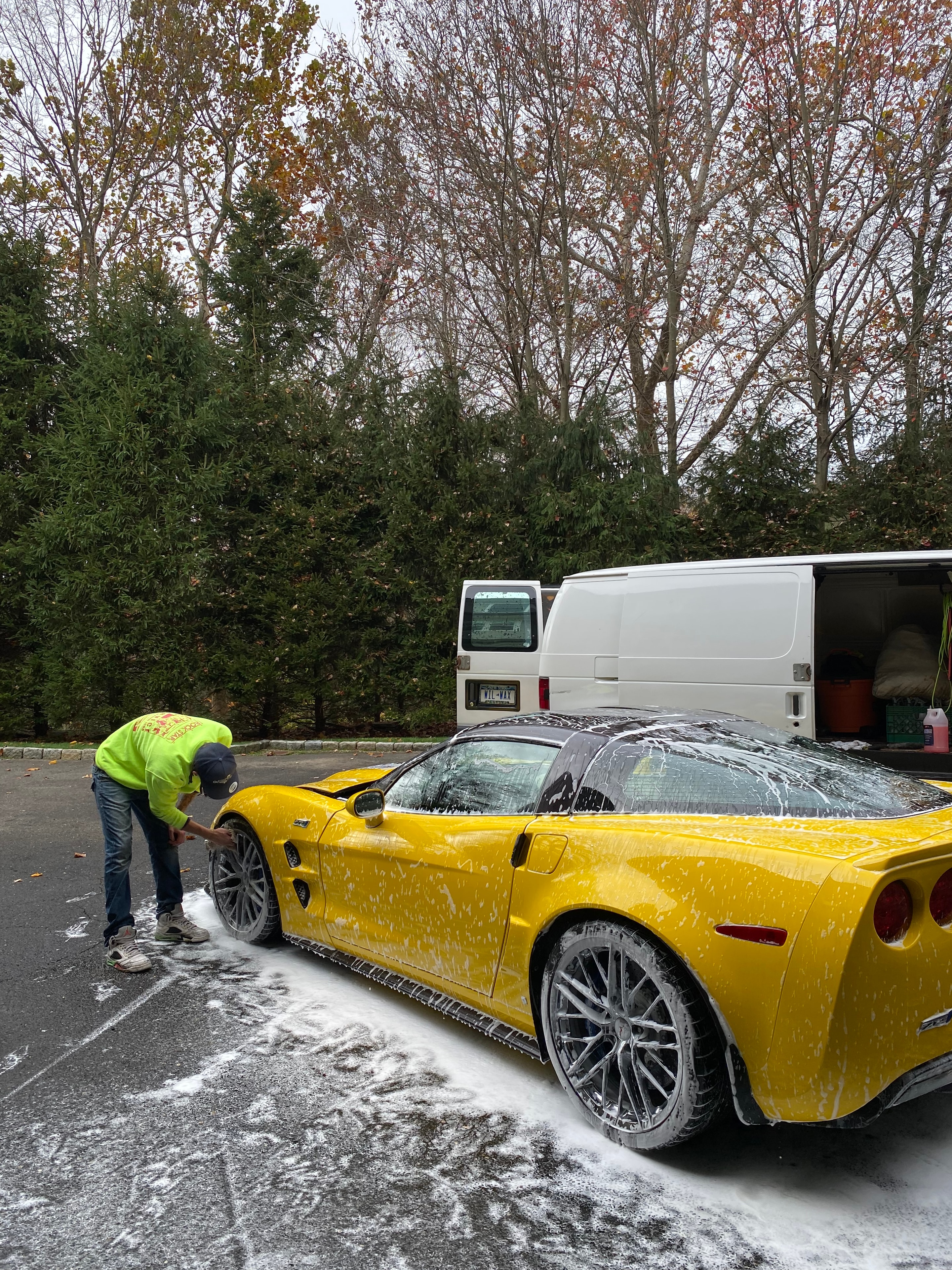 Wilson Waxes technician washing a yellow Corvette alongside the service van