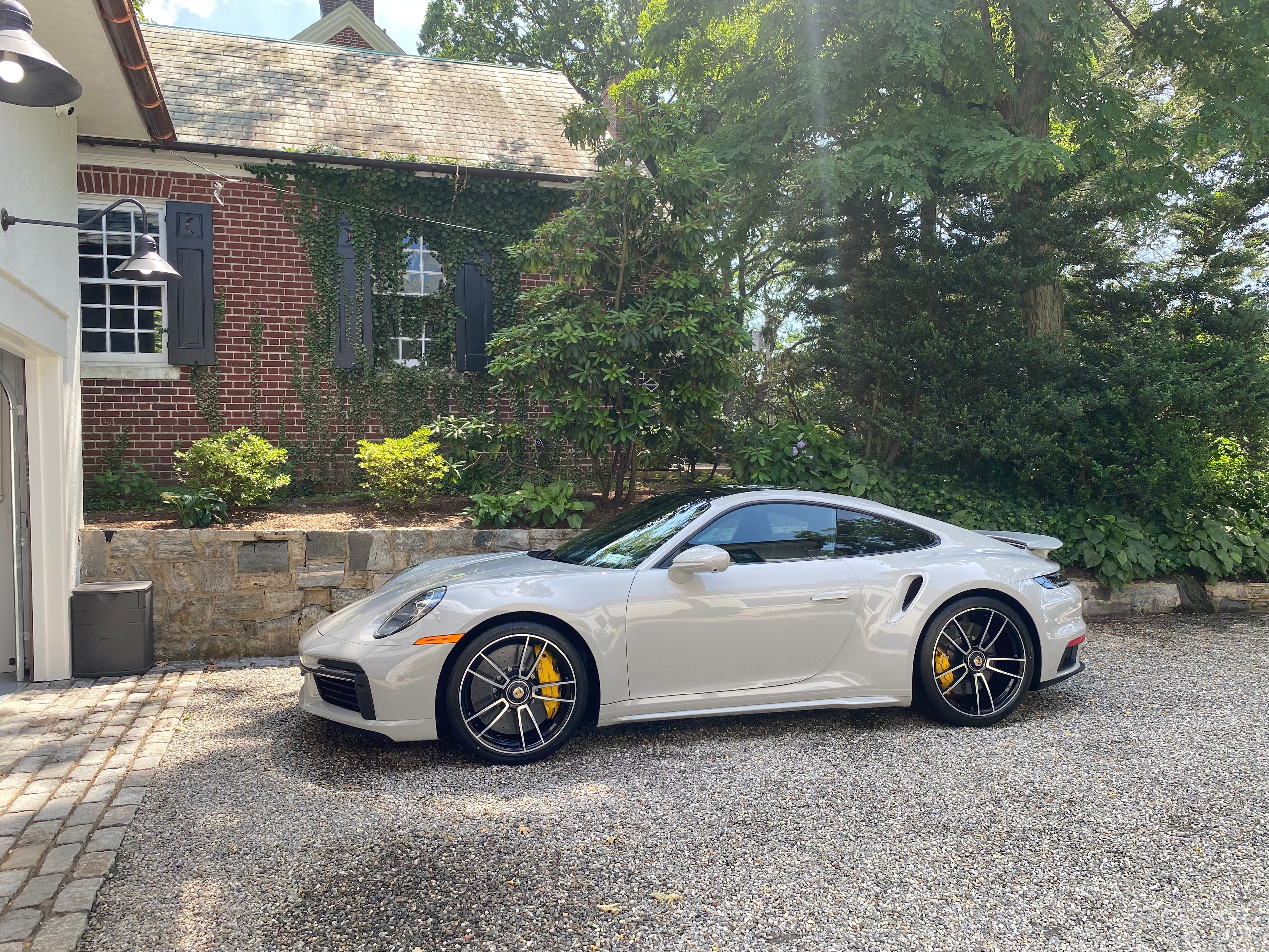 White Porsche 911 Turbo freshly detailed on a gravel driveway beside a brick estate