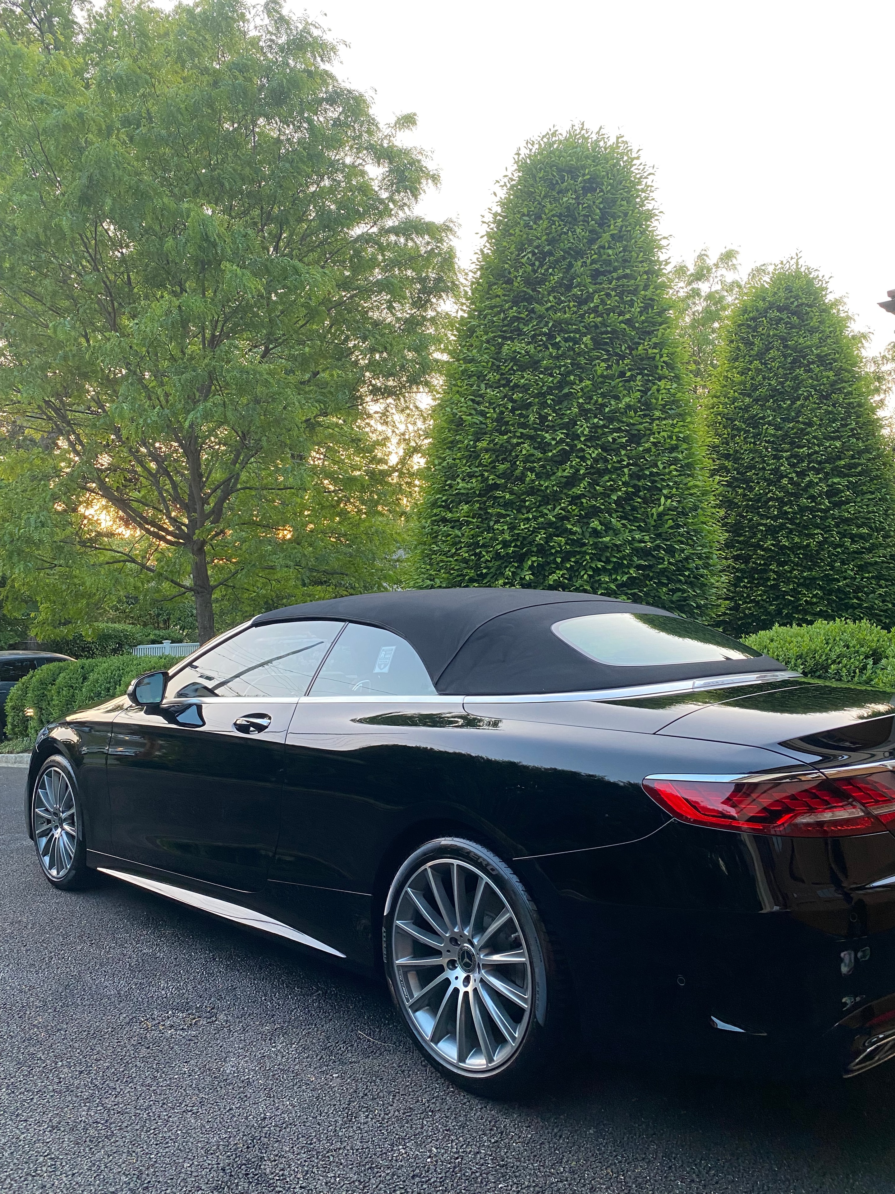 Black luxury sedan gleaming on a tree-lined Westchester street at golden hour