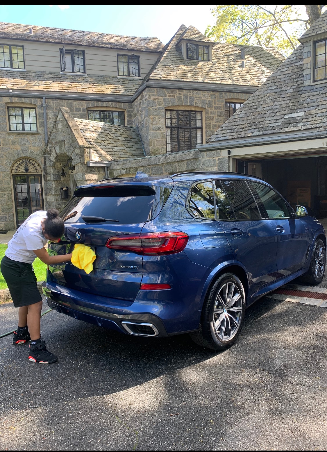 Wilson Waxes technician hand-drying a blue BMW X5 outside a stone estate