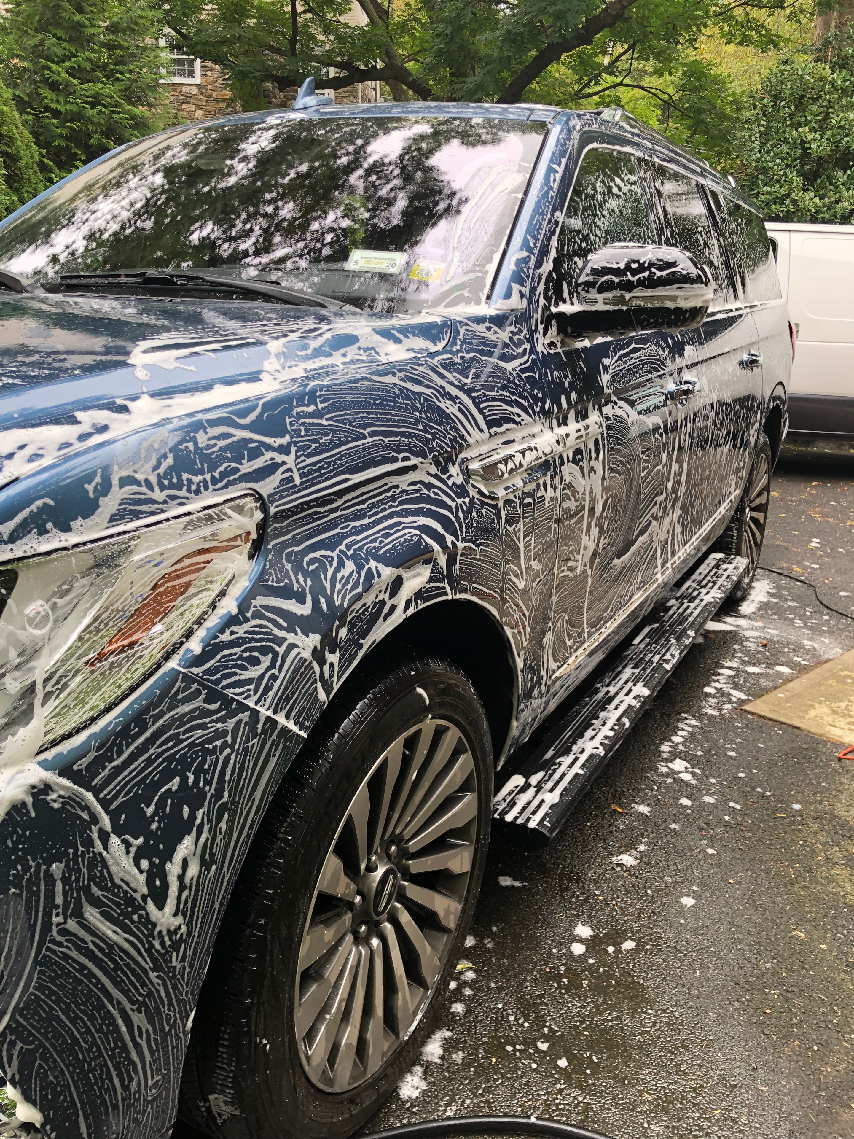 Dark blue SUV covered in foam being washed in a driveway